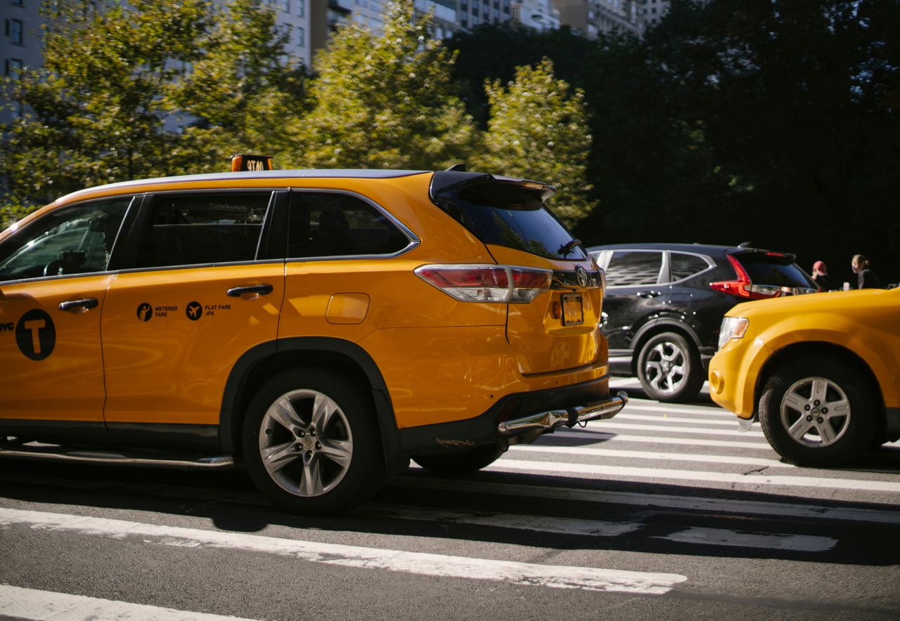 Yellow taxi cars and black SUV driving along road with pedestrian crossing in city centre on summer sunny day